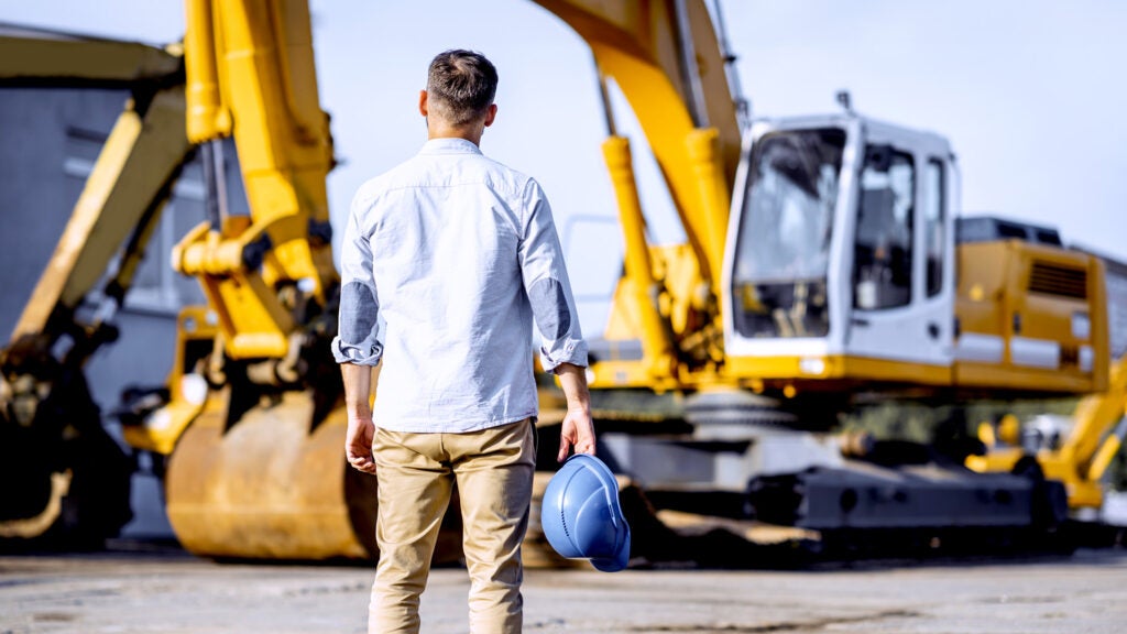 A business owner stands in front of a piece of heavy machinery.